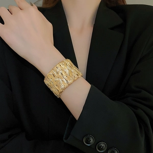 Detail of wide gold woven metal bangle cuff worn on wrist over a black blazer