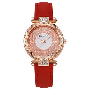 Close-up of rose gold watch with rhinestone bezel and red suede strap details