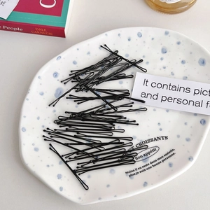 Set of classic black metal bobby pins scattered on a decorative plate for hairstyling
