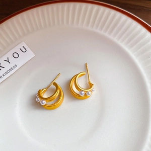 Detail of gold double-hoop earrings set with small pearls on a ceramic plate