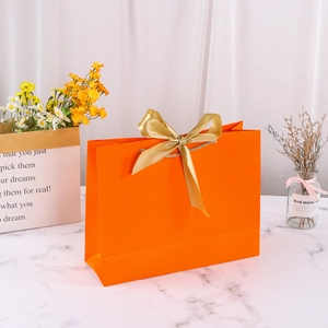 Orange paper gift bag featuring a wide gold satin ribbon bow and square bottom base