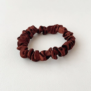 Detail shot of brown satin scrunchie showing glossy texture and elegant pleats on leather