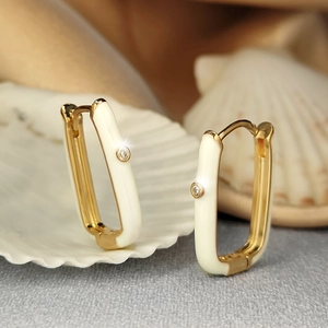 Close-up of gold-plated rectangular enamel earrings with zircon on a shell background