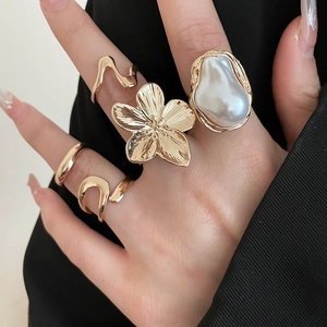 Detailed close-up of gold ring set with flower patterns and large baroque pearls on hand