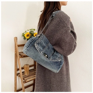 Detail of a dark blue denim crossbody bag with metal rivets and a silver chain strap