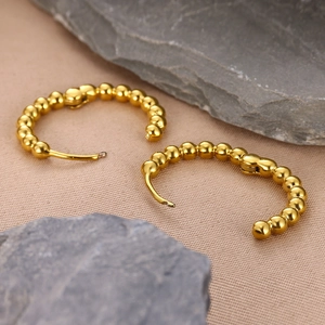 Close-up of gold beaded C-shape hoop earrings on textured fabric and grey stones