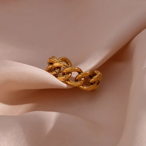 Macro shot of gold Cuban chain ring on soft pink silk fabric with metallic texture
