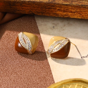 Close-up of geometric enamel stud earrings featuring brown and beige tiles with small diamonds