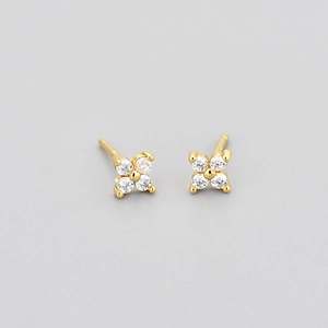 Close-up of gold stud earrings with four-petal floral design and clear cubic zirconia