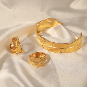 Gold feather jewelry set with open bangle and rings on premium white silk background