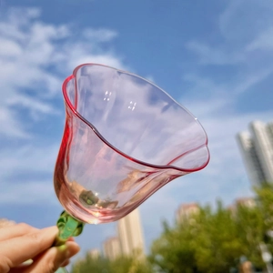 Pink tulip-shaped wine glass with green stem held against a blue sky background
