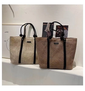 Detail view of woven straw tote bags in beige and brown with elegant black handles