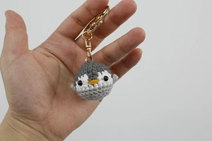 Close-up of handmade crochet penguin keychain with a golden lobster clasp on white background