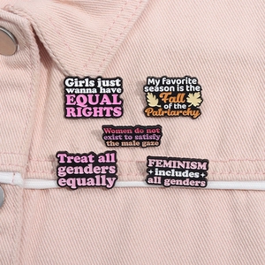 Detail von fünf Emaille-Pins mit Gleichheits-Slogans auf rosa Jeansstoff-Material
