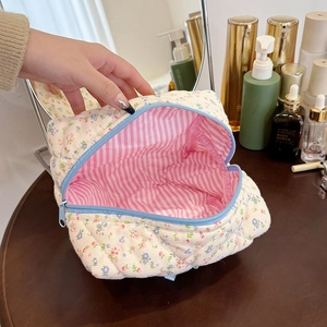 Quilted cotton cosmetic bag with floral print and blue zipper shown being held