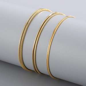 Three minimalist gold-plated snake bone chains wrapped on a grey cylinder display