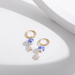 Detail view of gold hoop earrings with blue floral ceramic beads and baroque pearls