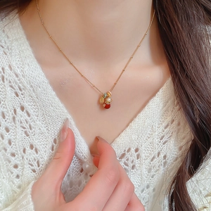 Close-up of gold-plated necklace with red agate, pearls and lucky bag charm on model