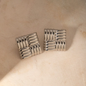 Macro shot of silver square textured earrings with a woven pattern on marble background