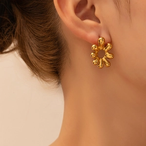 Close-up of a polished gold-plated stainless steel flower earring worn on an earlobe