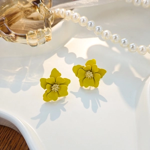 Macro detail of yellow layered petal flower earrings on white wavy jewelry tray