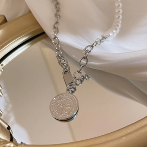 Detail of silver chain necklace with coin pendant and pearls on white silk backdrop