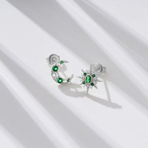Macro detail of asymmetric silver star and moon earrings with green and white zircons