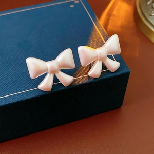 Macro shot of pearl white bow stud earrings with a silky luster on a dark blue jewelry box