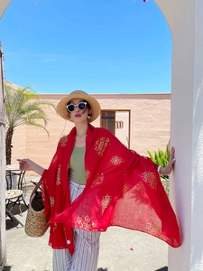 Detail of red beach shawl with gold mandala pattern framed by white arch and blue sky