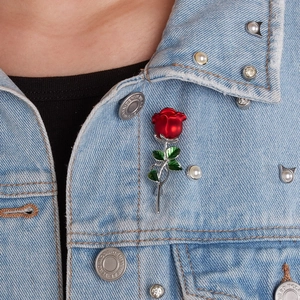Detail of red rose brooch with green leaves pinned on a light blue denim jacket