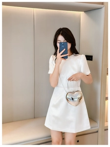 Silver heart-shaped acrylic bag with metal chain strap held by a model in a white dress