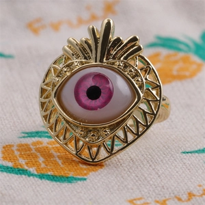 Macro shot of gold heart-shaped ring with pink evil eye stone on fabric background