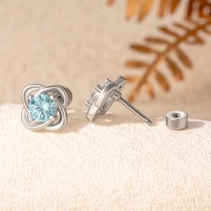 Silberne Kleeblatt-Ohrstecker mit blauem Zirkonia und Schraubverschluss auf Textur