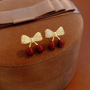 Gros plan de boucles d'oreilles cerise avec ruban doré et zircons sur boîte en velours