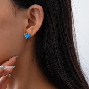 Close-up of a blue heart-shaped enamel stud earring worn by a model in soft light