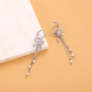 Détail de boucles d'oreilles nœud argentées avec perles blanches sur marbre