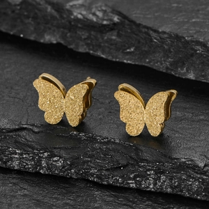 Macro shot of gold-plated butterfly stud earrings with matte frosted finish on slate