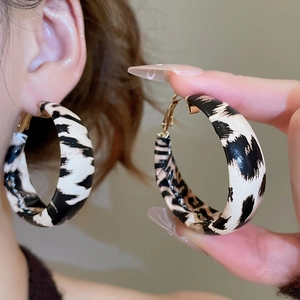 Detail of large hoop earrings featuring a modern black and white marbled leather texture