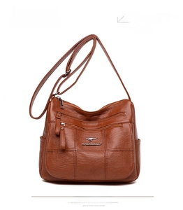 Detailed close-up of brown pebbled leather texture and front zipper pockets of the crossbody bag