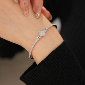 Close-up of zircon clover bracelet in silver finish worn on wrist over black cuff