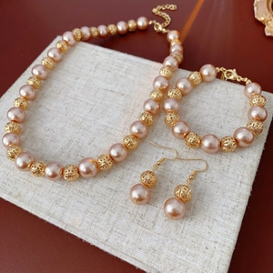 Three-piece pink pearl and gold metal jewelry set with necklace, bracelet, and earrings