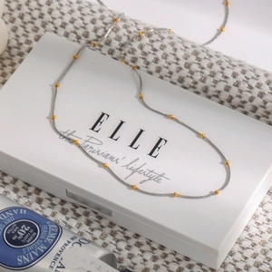 Detail of silver snake chain necklace with gold beads on a chic textured backdrop