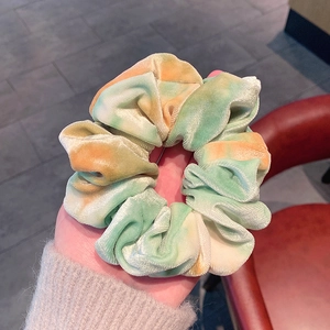 Detailed view of soft velvet scrunchie featuring vibrant green and orange tie-dye colors