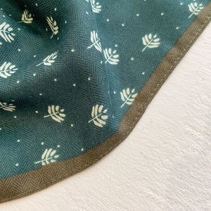 Detail of dark green printed silk scarf featuring herringbone weave and leaf patterns