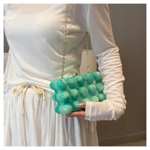 Détail de la pochette en acrylique vert à bulles avec chaîne dorée et fermoir sphérique
