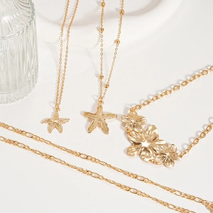 Gold starfish and flower pendant necklace set on a white tray with elegant glassware