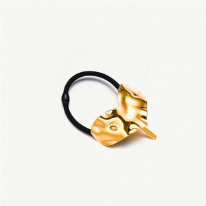 Macro detail of a wavy gold heart-shaped charm on a premium black elastic hair tie