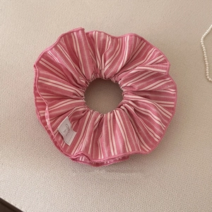 Gros plan du chouchou rayé rose et blanc avec étiquette nœud sur tissu beige doux