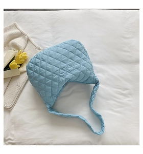 Flat lay of a light blue quilted puffer tote bag on white sheets with tulips