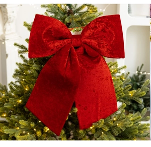Detail of a large red velvet bow ornament placed atop a Christmas tree with warm lights